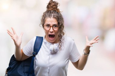 Sırt çantası ve kulaklık üzerinde giyen genç esmer öğrenci kız deli kutluyor arka plan izole ve başarı için kaldırdı kollarını açarak hayrete ve heyecanlı çığlık gözleri açık. Kazanan kavramı