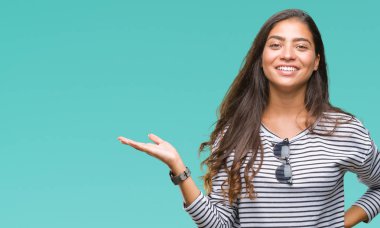 Genç güzel Arap kadın neşeli sunulması ve kameraya bakarak avucunun ile işaret gülümseyen izole arka plan üzerinde güneş gözlüğü takıyor.