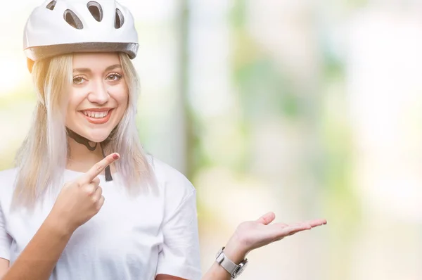 年轻的金发女子穿着自行车安全头盔在孤立的背景下 用手和手指指着脸 惊讶和微笑的相机 — 图库照片