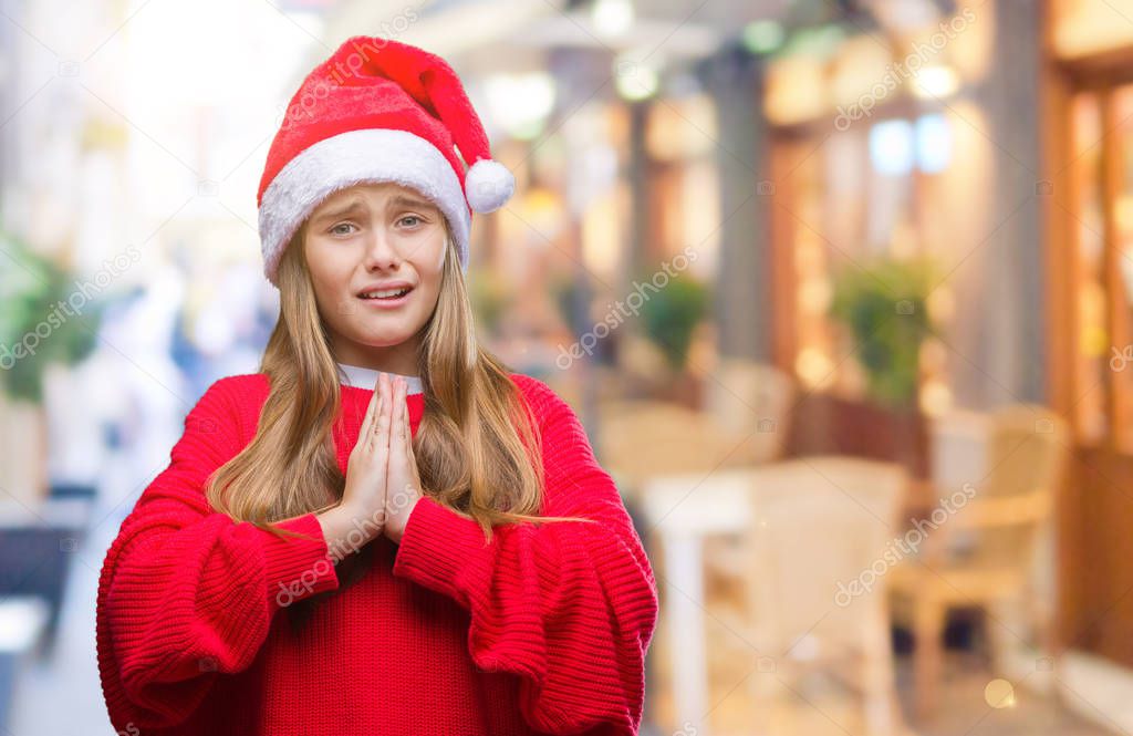Young beautiful girl wearing christmas hat over isolated background begging and praying with hands together with hope expression on face very emotional and worried. Asking for forgiveness. Religion concept.