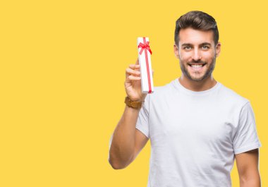 Sevgililer hediye izole arka plan üzerinde duran ve diş gösterilen kendine güvenen bir gülümsemeyle gülümseyerek mutlu bir yüz ile veren aşık genç yakışıklı adam