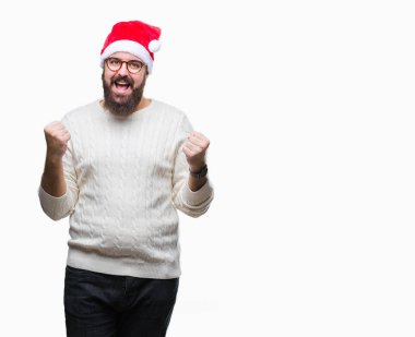 Noel şapka ve gözlük izole arka plan kutlama üzerinde giyen genç beyaz adam şaşırttı ve başarı için kaldırdı kollarını açarak hayret ve gözleri açık. Kazanan kavramı.