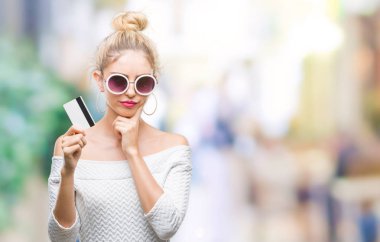 İzole arka plan ciddi bir yüz düşünme hakkında soru, çok karışık fikir üzerinden kredi kartı tutan genç güzel sarışın kadın