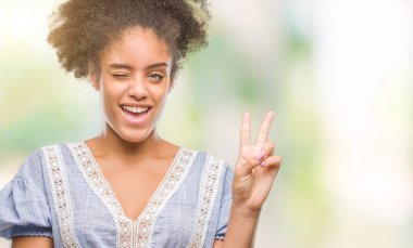 Mutlu yüz zafer işareti yaparken kameraya göz kırpıyor ile gülümseyen izole arka plan üzerinde genç afro Amerikalı kadın. İki numaralı.