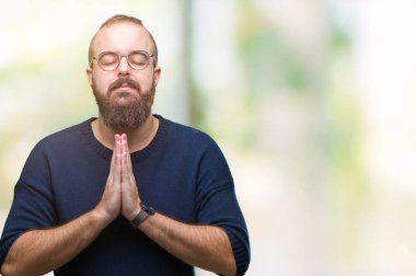 Genç beyaz hipster adam eliyle birlikte AF emin gülümseyen için soran dua izole arka plan üzerinde güneş gözlüğü takıyor.