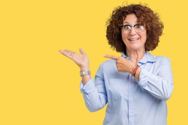 Hayret ve el ile sunulması ve parmak ile işaret ederken kameraya gülümseyen izole arka plan üzerinde gözlük güzel orta ager üst düzey businees kadın.