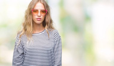 Yüzünde ciddi bir ifade ile izole arka plan üzerinde güneş gözlüğü takıyor güzel sarışın genç kadın. Basit ve doğal kameraya bakıyor.