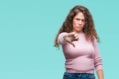 Güzel esmer kıvırcık saçlı Genç kız mutsuz ve kızgın ret gösterilen ve başparmak aşağı hareketi ile negatif seyir izole arka plan üzerinde pembe kazak giyiyor. Kötü ifade.