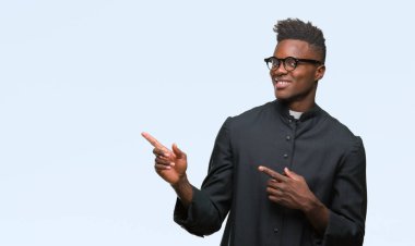 Genç Afro-Amerikan rahip adam gülümseyerek ve iki elleri ve parmakları ile tarafına işaret kamera bakarak izole arka plan.
