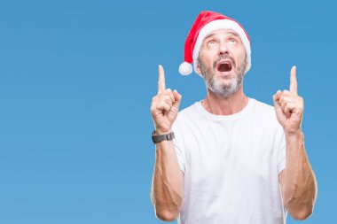 Noel şapka izole arka plan üzerinde orta yaş ağarmış komuta sizde hayrete ve yukarıya bakıyor ve parmakları ile işaret ve silah kaldırdı şaşırttı.