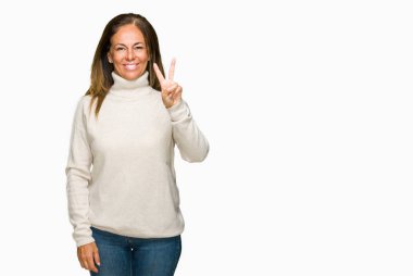 Güzel orta yaş yetişkin kadın giyiyor kış kazak gösterilen ve parmakları ile işaret izole arka plan üzerinde ikincisi ise kendinden emin ve mutlu gülümseyerek.