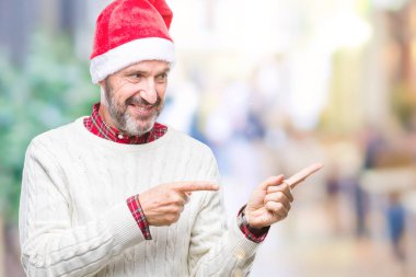 Orta yaş ağarmış komuta sizde gülümseyen ve iki elleri ve parmakları ile tarafına işaret kamera bakarak izole arka plan üzerinde Noel şapka.