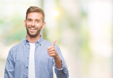 Hareketi el ile mutlu yaşasın yapıyor izole arka plan üzerinde beyaz t-shirt giyen genç yakışıklı adam. Kameraya bakarak başarı gösteren ile ifade onaylama.