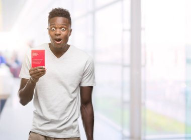 İsviçre pasaportu bir sürpriz yüz, korkuyor ve heyecanlı korku ifadesi ile şok korkmuş tutan genç Afro-Amerikan adam