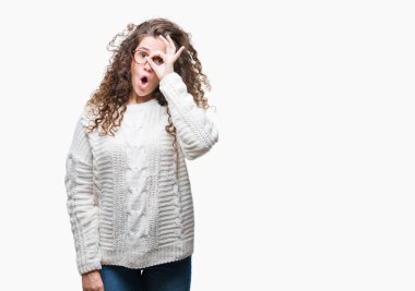 Güzel esmer kıvırcık saçlı Genç kız ok jest sürpriz yüz, göz parmaklarının arasından seyir şok yapıyor izole arka plan üzerinde kış kazak giyiyor. İmansız ifade.