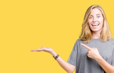 Hayret ve el ile sunulması ve parmak ile işaret ederken kameraya gülümseyen izole arka plan üzerinde büyük boy rahat t-shirt giyen güzel genç kadın.