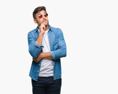 Genç yakışıklı adam çene düşünme hakkında soru, dalgın ifade üzerine el ile izole arka plan üzerinde güneş gözlüğü takıyor. Düşünceli yüzüyle gülümsüyor. Şüphe kavramı.