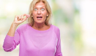 Orta yaş sarışın kadın üzerinde pembe macaron bisküvi yediğine arka plan bir sürpriz yüz, korkuyor ve heyecanlı korku ifadesi ile şok korkmuş izole