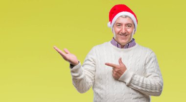 Üst düzey yakışıklı Noel şapka üzerinden hayran ve el ile sunulması ve parmak ile işaret ederken kameraya gülümseyen izole arka plan.