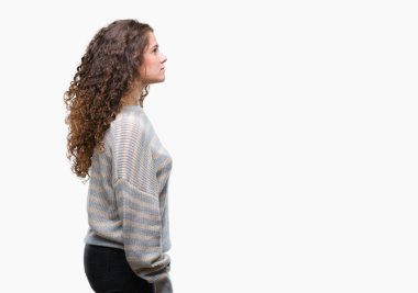 Güzel esmer kıvırcık saç üzerinde kış kazak giyen genç kız tarafına, seyir arka plan izole dinlenmek doğal yüz emin gülümseme ile pozuyla profili.