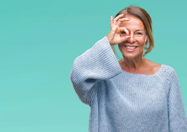 Gülümseyen, parmakları ile mutlu yüz üzerinden seyir göz el ile ok jest yapıyor izole arka plan üzerinde kış kazak giyen orta yaş üst düzey İspanyol kadın.