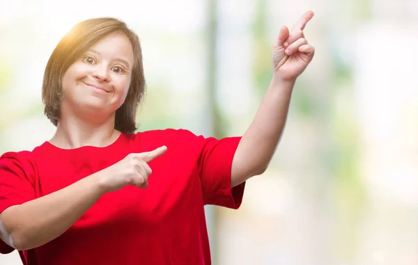 Young adult woman with down syndrome over isolated background smiling and looking at the camera pointing with two hands and fingers to the side.