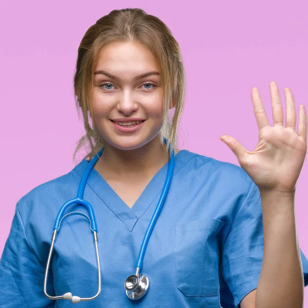 上外科医制服を着て若い白人医師女性分離を示す背景と自信を持って 幸せな笑みを浮かべて 指で上向きナンバーファイブ — ストック写真