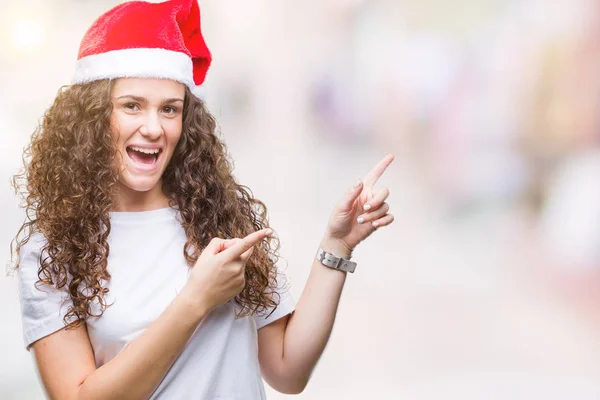 年轻的黑发女孩戴着圣诞帽在孤立的背景微笑着 看着相机指向与两个手和手指的一侧 — 图库照片