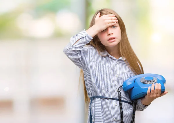 Young blonde toddler holding vintage telephone stressed with hand on head, shocked with shame and surprise face, angry and frustrated. Fear and upset for mistake.