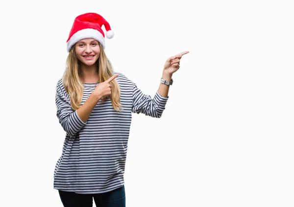 笑顔で側に つの手と指で指しているカメラを見て孤立の背景にクリスマスの帽子をかぶって若い美しいブロンドの女性 — ストック写真