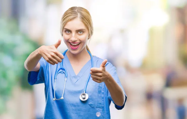 若い美しい金髪医師外科医看護師女性の手で肯定的なジェスチャーをして承認する分離の背景の上の親指を笑顔と幸せな成功のため カメラ 勝者のジェスチャーを見てください — ストック写真