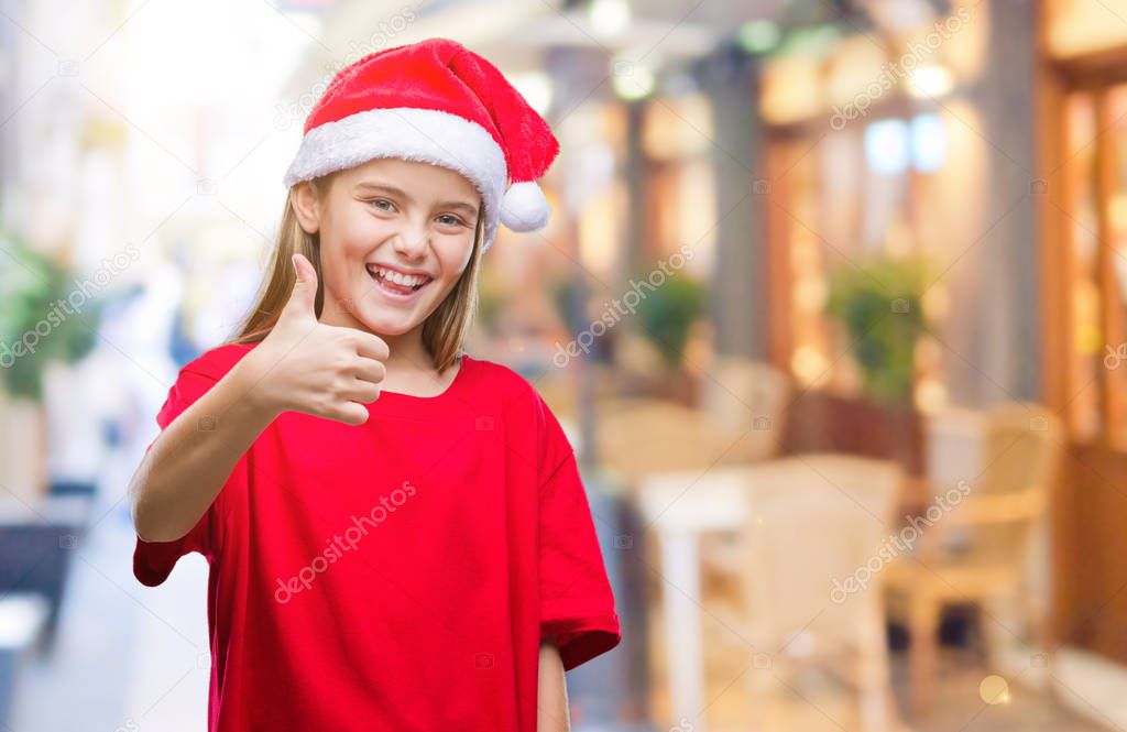 Young beautiful girl wearing christmas hat over isolated background doing happy thumbs up gesture with hand. Approving expression looking at the camera with showing success.