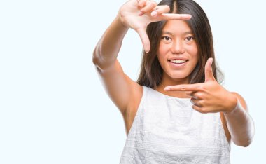 Genç Asyalı kadın elle yapma çerçeve ve parmakları ile mutlu yüz gülümseyen izole arka plan üzerinde. Yaratıcılık ve Fotoğrafçılık kavramı.