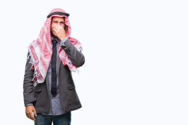 Genç yakışıklı Arap adam uzun saçlı keffiyeh bir şey pis ve iğrenç kokulu izole arka plan üzerinde dayanılmaz koku, holding nefes parmak ile burnuna giyiyor. Kötü kokuyor kavramı.