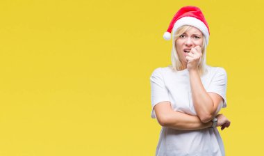 Stresli ve gergin elle çivi ısırma ağzına bakarak izole arka plan üzerinde Noel şapka giyen genç güzel sarışın kadın. Anksiyete sorunu.
