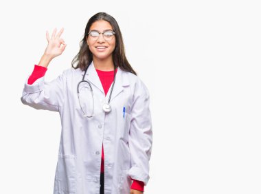 İzole arka plan el ve parmaklar ok işaretiyle yapıyor olumlu gülümseyen üzerinde genç Arap doktor kadın. Başarılı ifade.