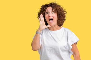 Bağırarak ve ağzı üzerinde el ile yan için çığlık izole arka plan üzerinde beyaz t-shirt giyen güzel orta ager kadın kıdemli. İletişim kavramı.