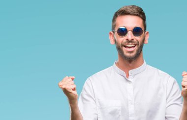 Yakışıklı delikanlı izole arka plan üzerinde kutluyor gözlük takan şaşırttı ve başarı için kaldırdı kollarını açarak hayret ve gözleri açık. Kazanan kavramı.