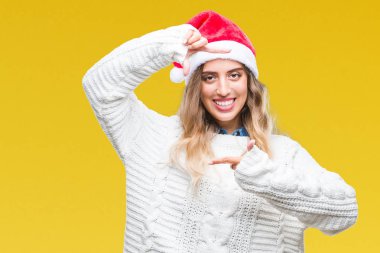 Elle yapma çerçeve ve parmakları ile mutlu yüz gülümseyen izole arka plan üzerinde Noel şapka giyen güzel genç sarışın kadın. Yaratıcılık ve Fotoğrafçılık kavramı.