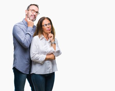 Orta yaş üzerinde gözlük takan aşık İspanyol çift çene düşünme hakkında soru, dalgın ifade üzerine el ile arka plan izole. Düşünceli yüzüyle gülümsüyor. Şüphe kavramı.