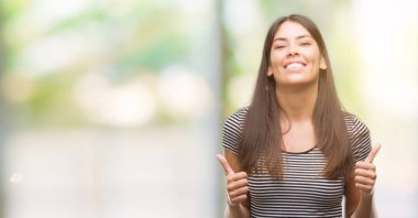 Genç güzel İspanyol kadın başarı işareti başparmak gülümseyen ve mutlu el ile olumlu hareketi yapıyor. Neşeli bir ifadeyle, kazanan jest kameraya bakıyor.