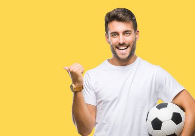 İşaret ve başparmak kadar mutlu yüz gülümseyen tarafı ile gösteren izole arka plan üzerinde futbol futbol topu tutan genç yakışıklı adam