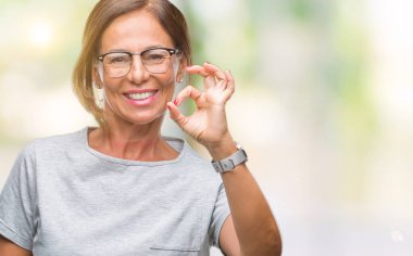 İzole arka plan el ve parmaklar ok işaretiyle yapıyor olumlu gülümseyen üzerinde gözlük takan orta yaş İspanyol kadın kıdemli. Başarılı ifade.