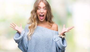 Üzerinde kış kazak giyen güzel genç sarışın kadın deli kutluyor arka plan izole ve başarı için kaldırdı kollarını açarak hayrete ve heyecanlı çığlık gözleri açık. Kazanan kavramı