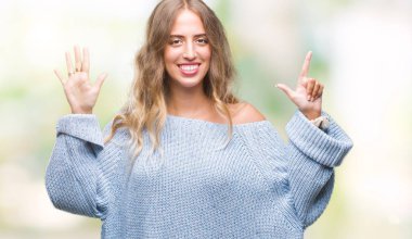 Güzel sarışın genç kadın giyiyor kış kazak gösterilen ve parmakları ile işaret izole arka plan üzerinde kendinden emin ve mutlu gülümseyerek süre yedi numara.