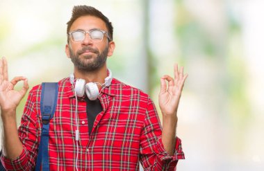 Kulaklıklar ve sırt çantası izole arka plan üzerinde giyen yetişkin İspanyol öğrenci adam rahatla ve gülümseyen gözlerle parmak ile meditasyon jest yapıyor kapalı. Yoga kavramı.