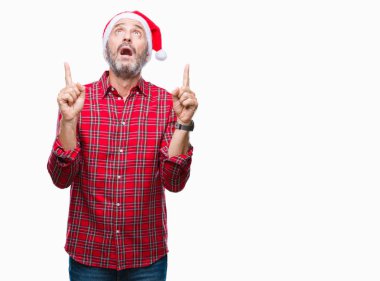 Noel şapka izole arka plan üzerinde orta yaş ağarmış komuta sizde hayrete ve yukarıya bakıyor ve parmakları ile işaret ve silah kaldırdı şaşırttı.