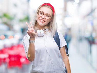 Mutlu yüz zafer işareti yaparken kameraya göz kırpıyor ile gülümseyen izole arka plan üzerinde gözlük ve sırt çantası giyen genç sarışın öğrenci kadın. İki numaralı.