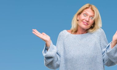 İzole arka plan clueless ve şaşkın bir ifadeyle kollar ve eller kaldırdı üzerinde kış kazak giyen orta yaş sarışın kadın. Şüphe kavramı.