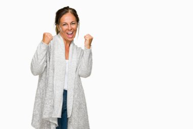 Üzerinde kış kazak giyen güzel orta yaş yetişkin kadın gülümseyerek ve başarı için çığlık arka plan çok mutlu ve heyecanlı kaldırdı, silah ile kazanan jest yapıyor izole. Kutlama kavramı.